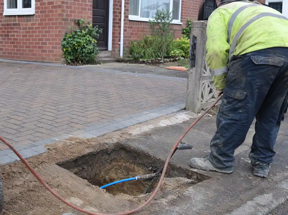 Moling launch pit beside an untouched block-paved drive in Nottingham, with an air hose and new blue water pipe