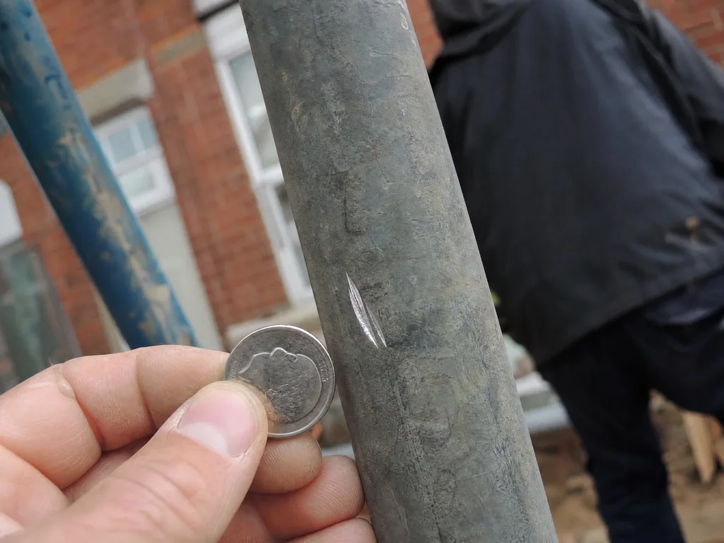 Old lead water pipe scratched with a coin to show bright silver metal, Nottingham